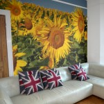 Fototapete bedruckt mit einem Foto von einem Sonnenblumenfeld, davor ein Sofa mit Kissen